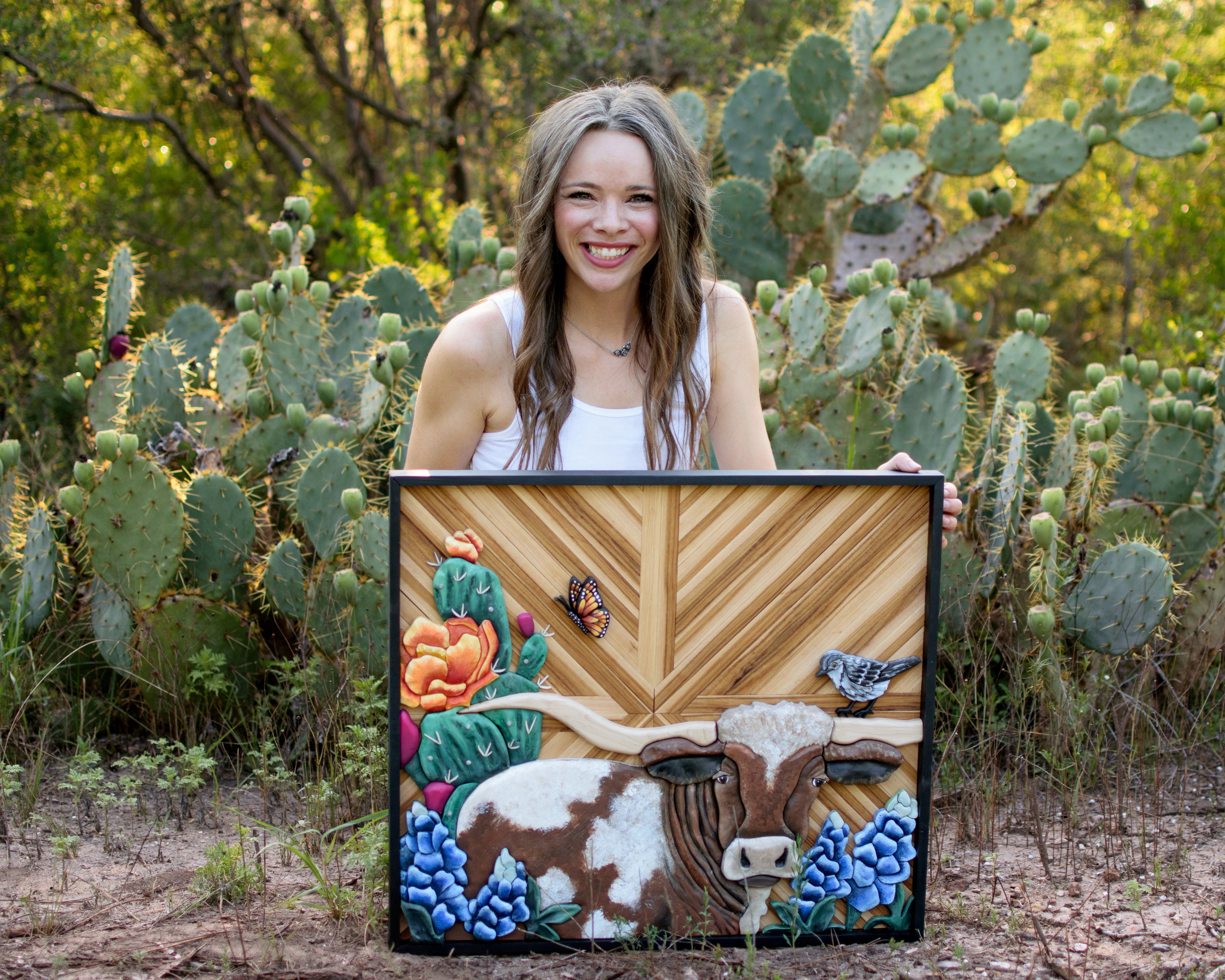 Person holding a decorated sign with a cow design in a desert setting